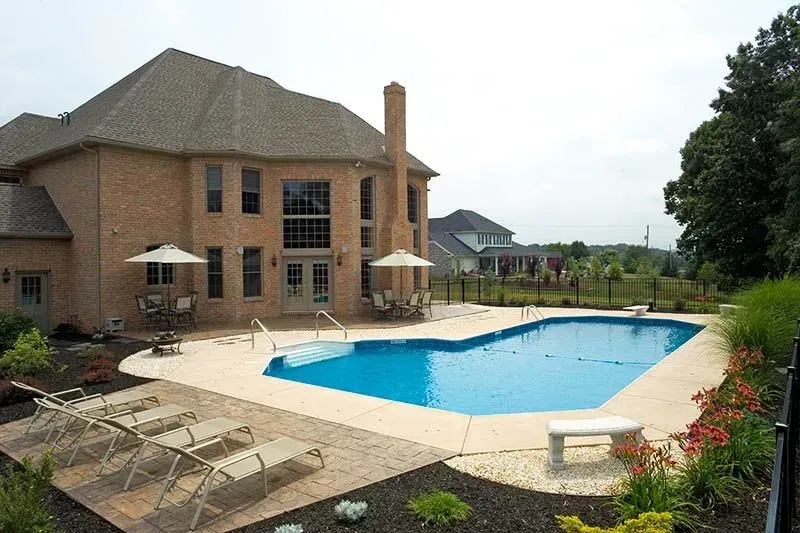 Backyard pool with a brick house and lounge chairs.