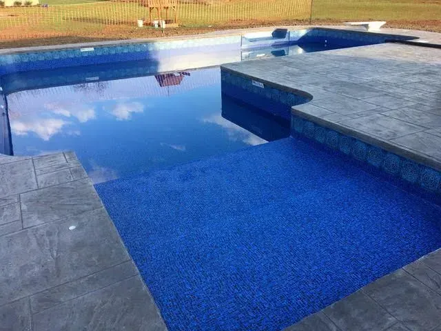 Blue tiled swimming pool with concrete decking, reflecting the sky.