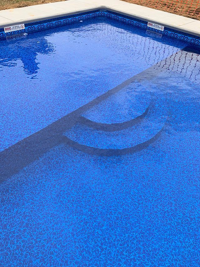 Blue tiled swimming pool with built-in steps, reflecting sunlight.