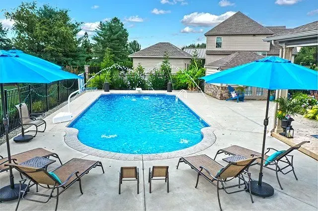 Pool with blue water and umbrellas, surrounded by lounge chairs and a house on a sunny day.