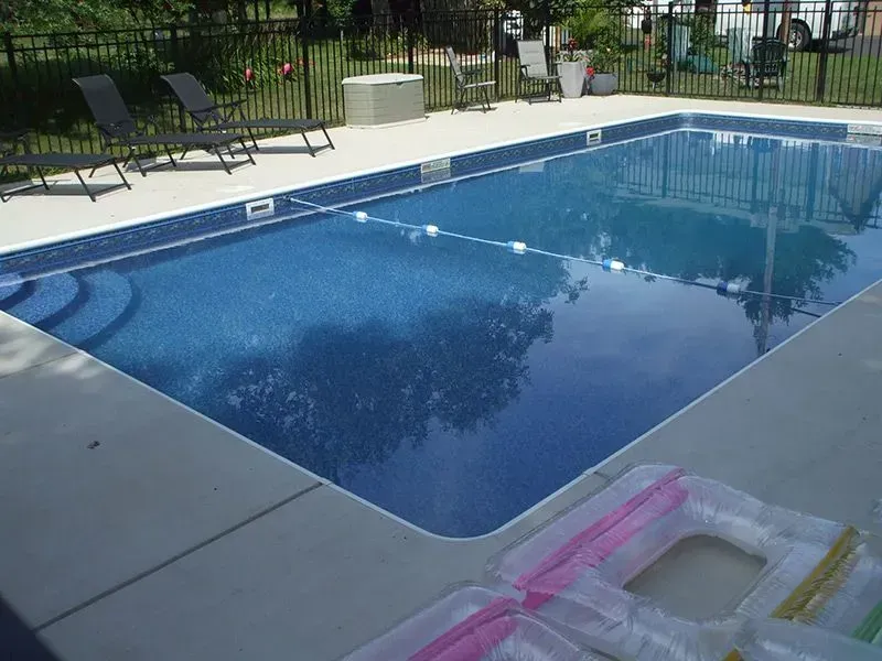 Rectangular swimming pool with blue tiled interior, white border, and pool toys on the side.
