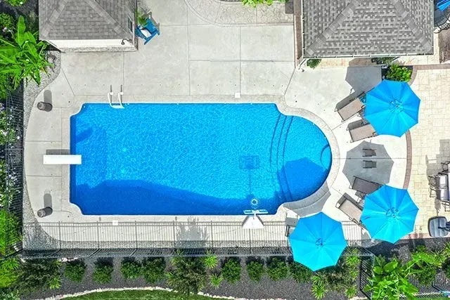 Overhead view of a swimming pool with blue water, surrounded by concrete and lounge chairs with blue umbrellas.