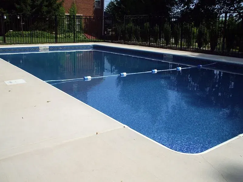 A rectangular swimming pool with blue water and light-colored concrete border.