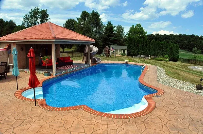 Pool with patterned blue tile, tan stamped concrete patio, and a covered patio area under a red tiled roof.