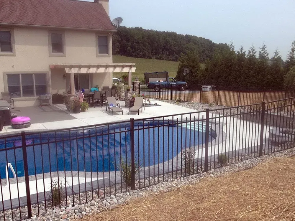 Black fence surrounds a backyard pool with a house and patio visible.