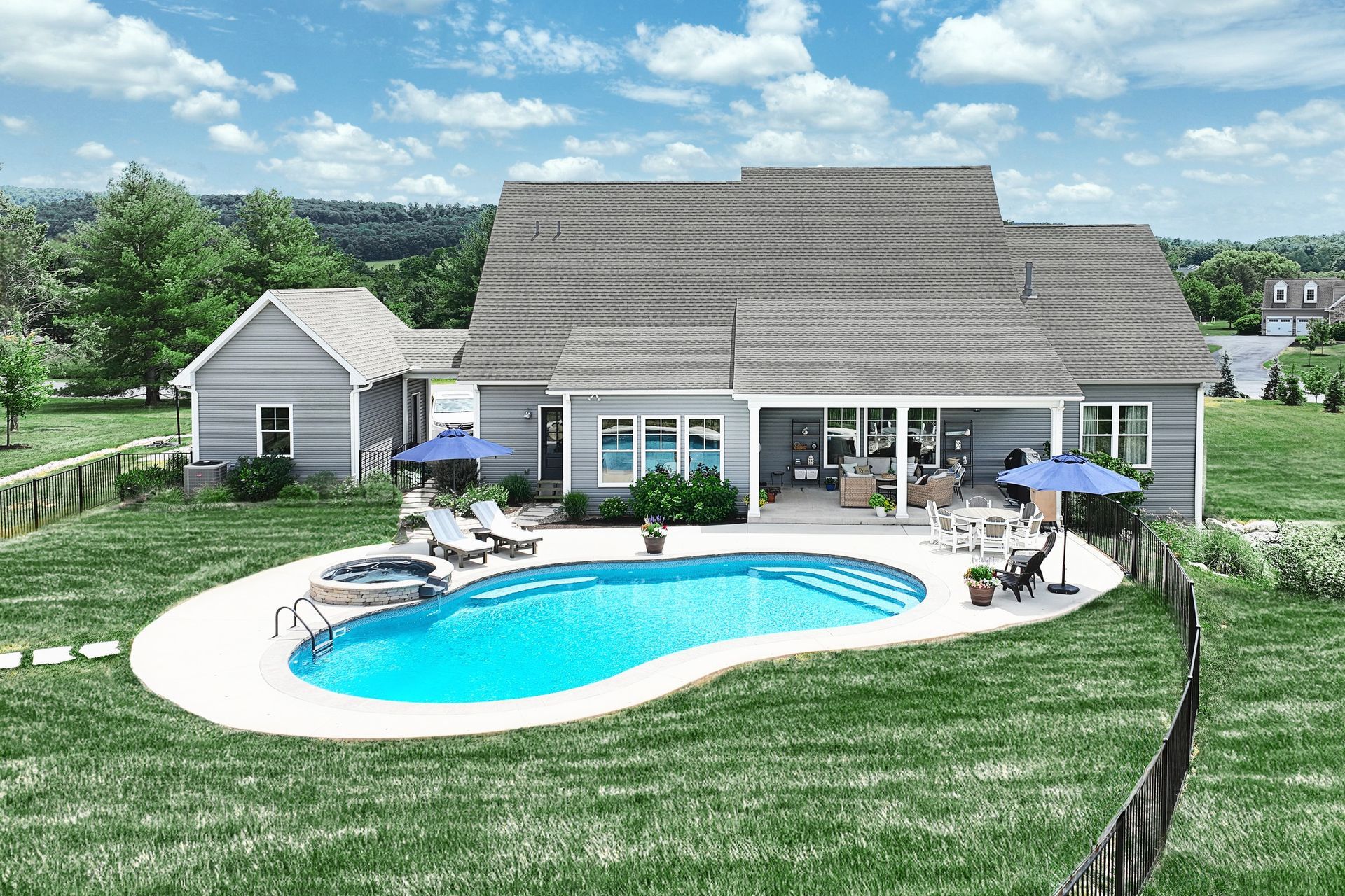 Backyard with pool, patio, and gray house under a blue sky.