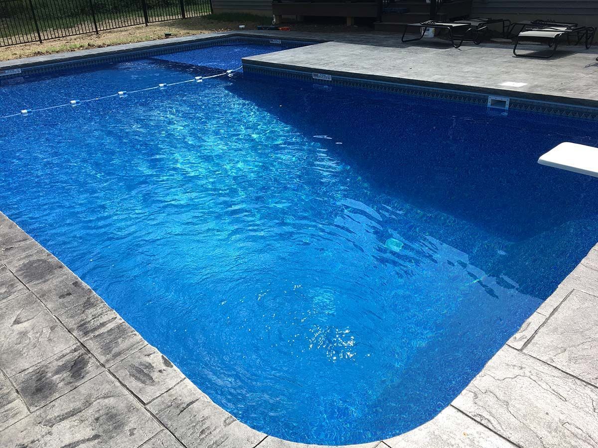 Blue rectangular pool with curved end, surrounded by gray concrete, partially covered.