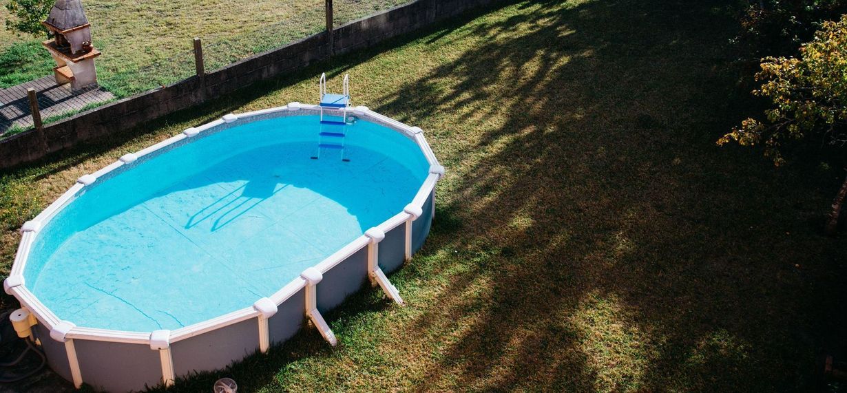 An oval above-ground swimming pool filled with water sits in a grassy yard.