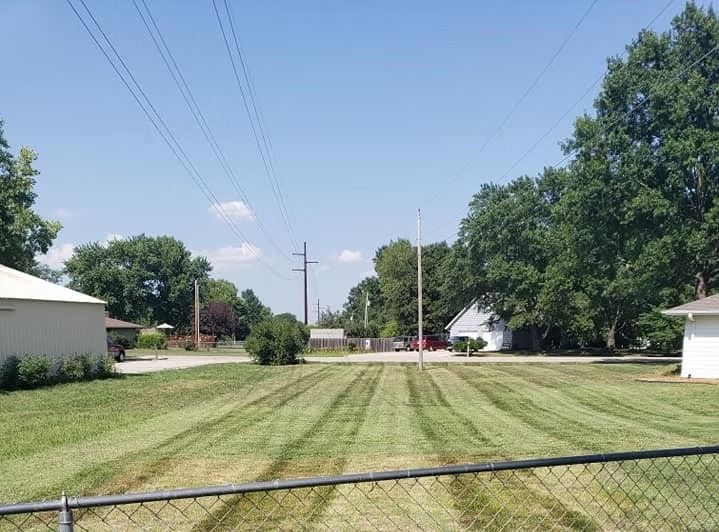 Lawn mowed in stripes in front of houses and trees under a blue sky, with power lines overhead.
