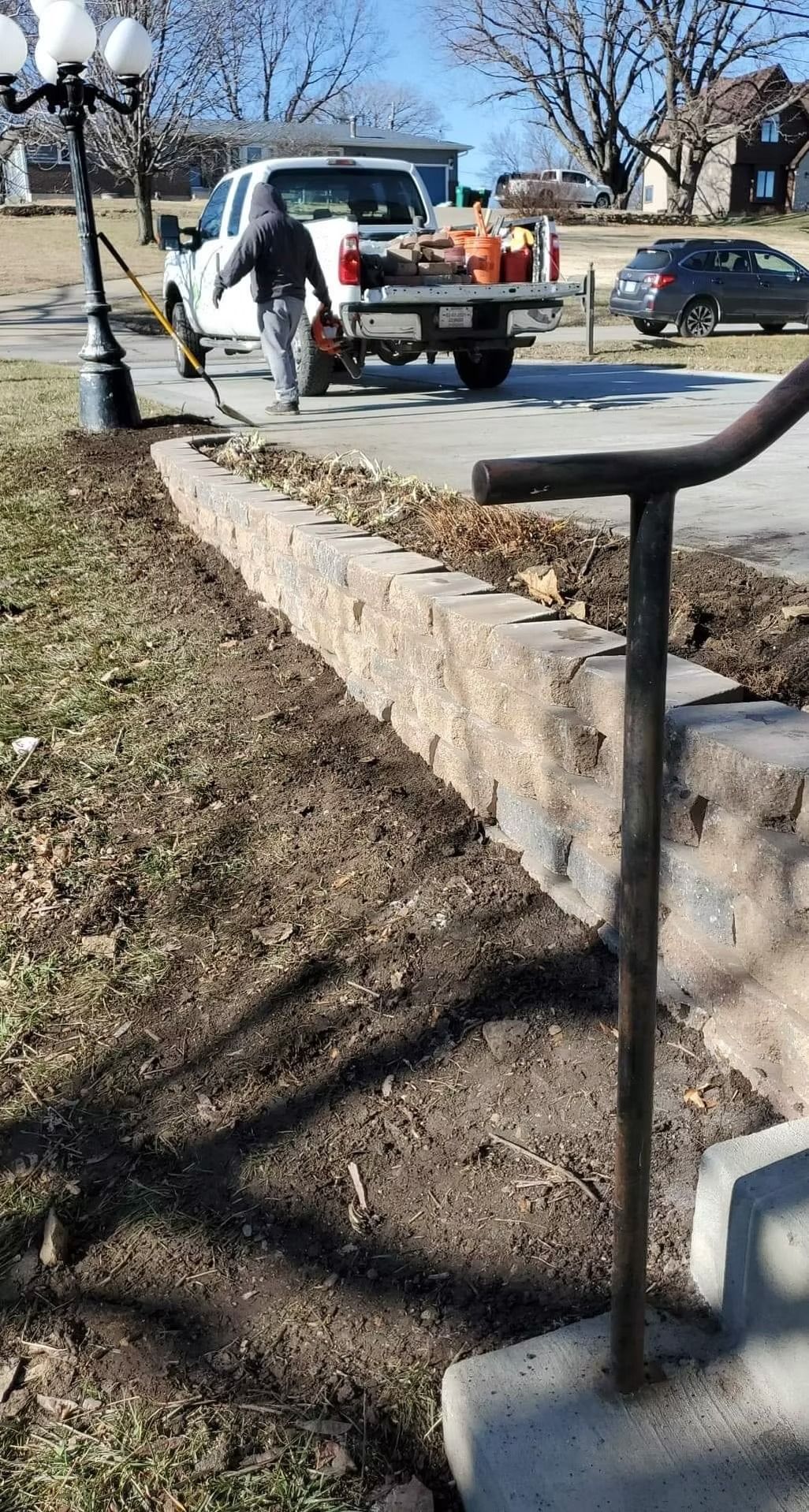 Man walking toward a truck parked near a stone retaining wall and grass.