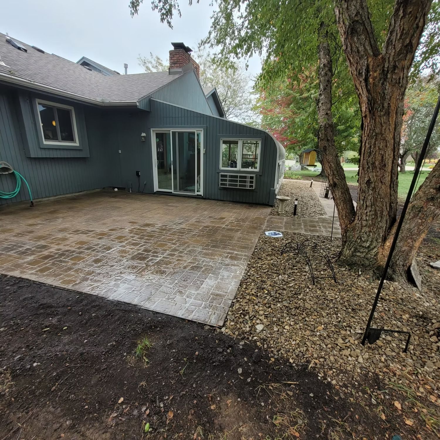 Gray house with patio, tree, and landscaping. Overcast day.