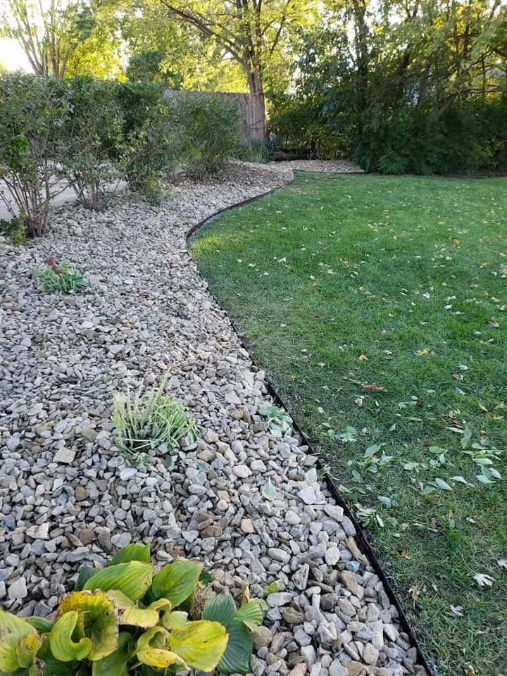 Stone and plant border alongside a green lawn, with trees in the background.