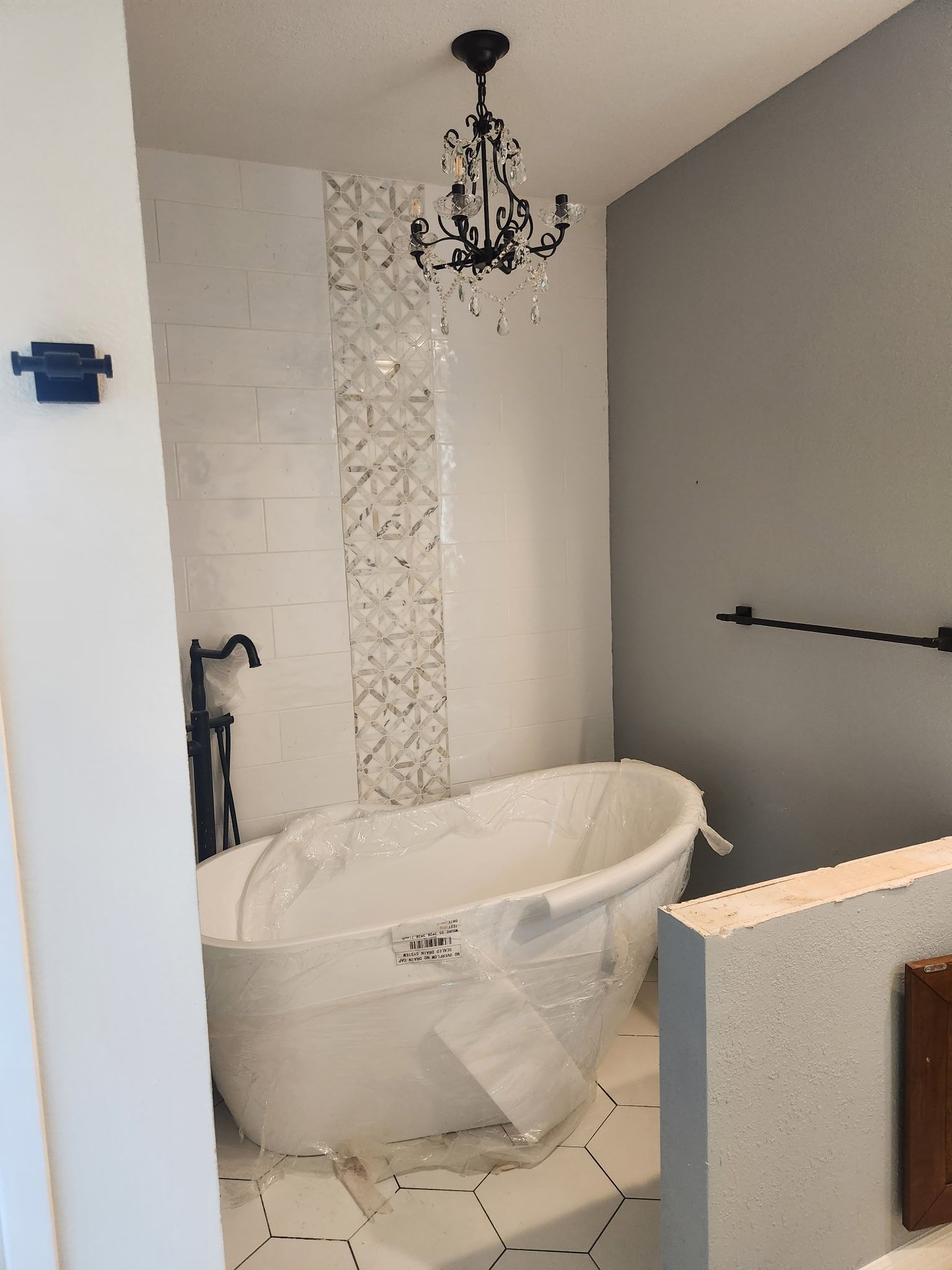 Bathroom with a white clawfoot tub, chandelier, and patterned tile.