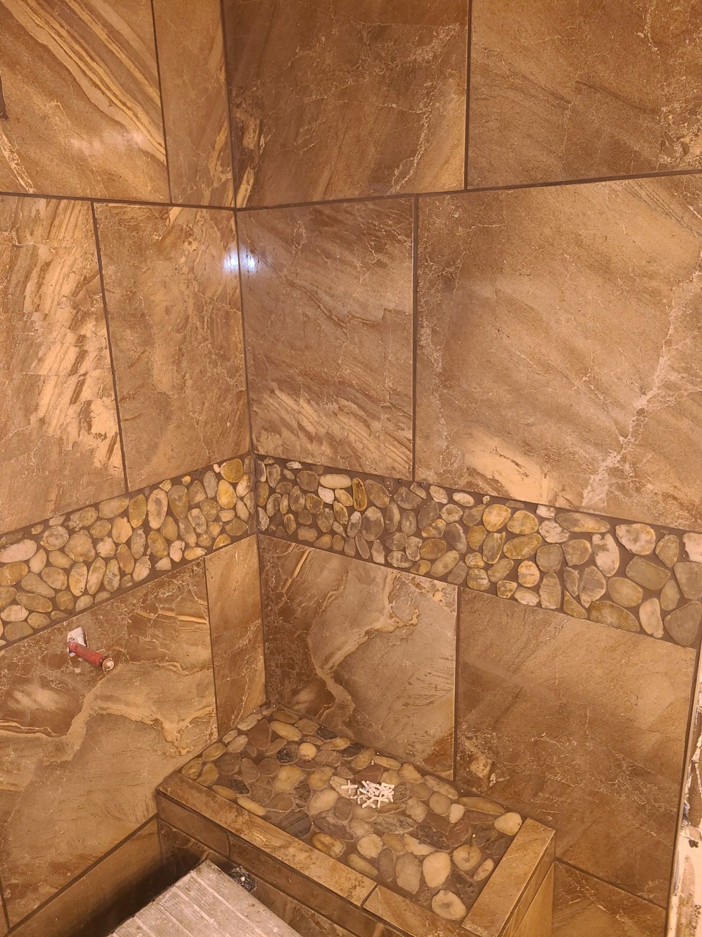 Brown tile shower with a band of river rock tile. A small bench is also tiled with river rocks.