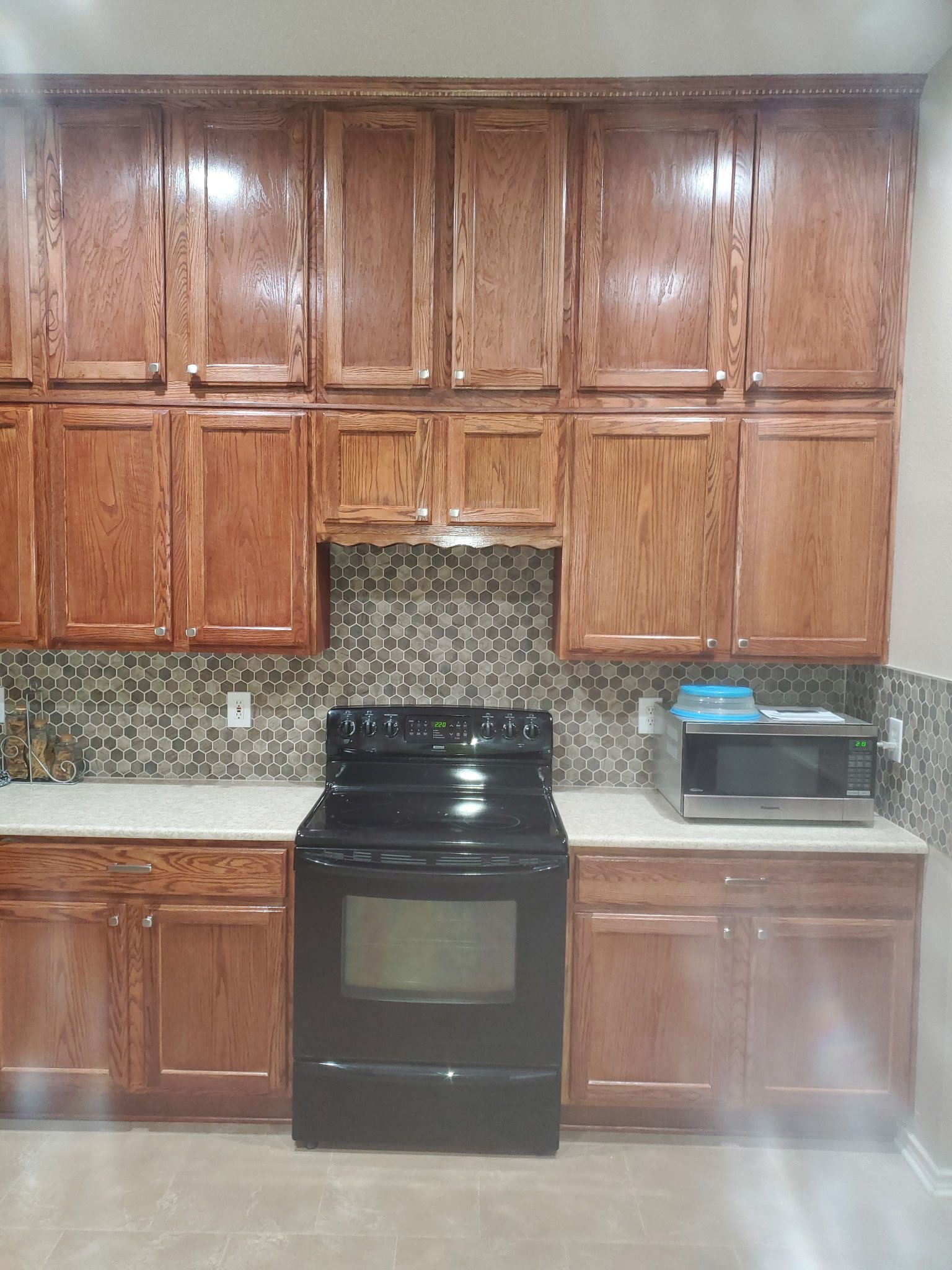 Kitchen with brown cabinets, black stove, microwave, and patterned backsplash.