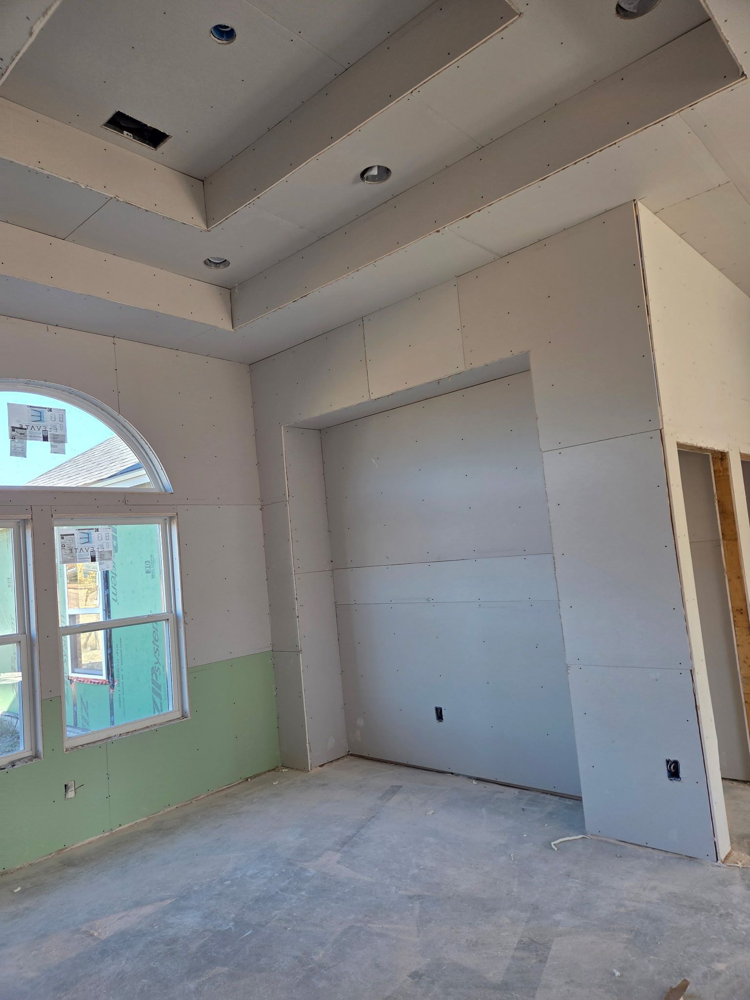 Interior room under construction with drywall installed. Arch window, recessed ceiling lights, and built-in alcove.