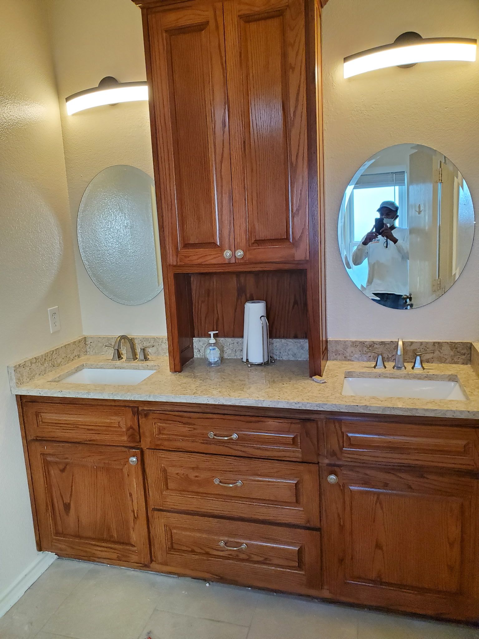 Bathroom with brown wooden cabinets, granite countertop, oval mirrors, and overhead lighting.