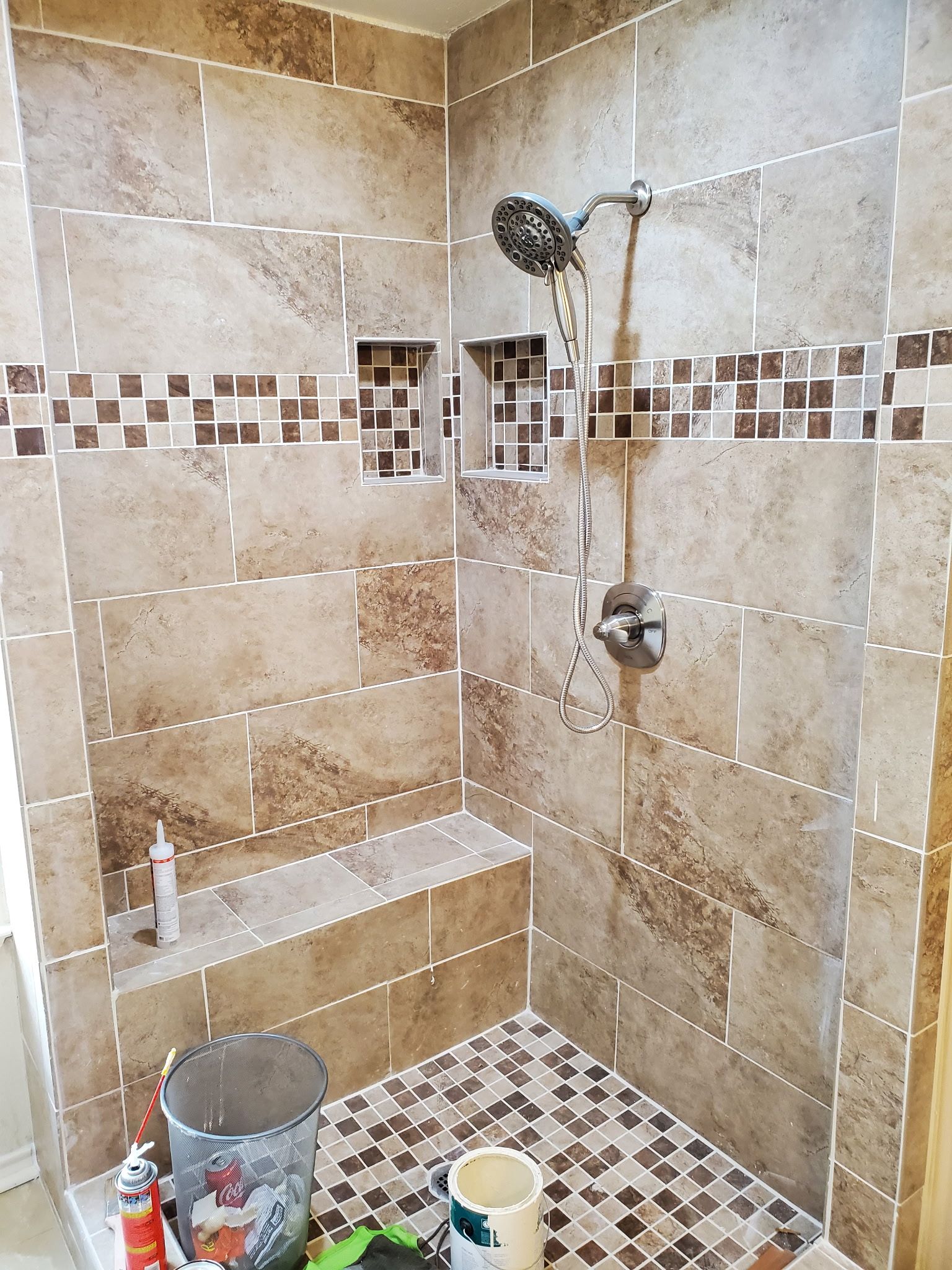 Tiled shower with built-in bench and mosaic accents. Brown and beige tiles, shower head, and small storage niches.