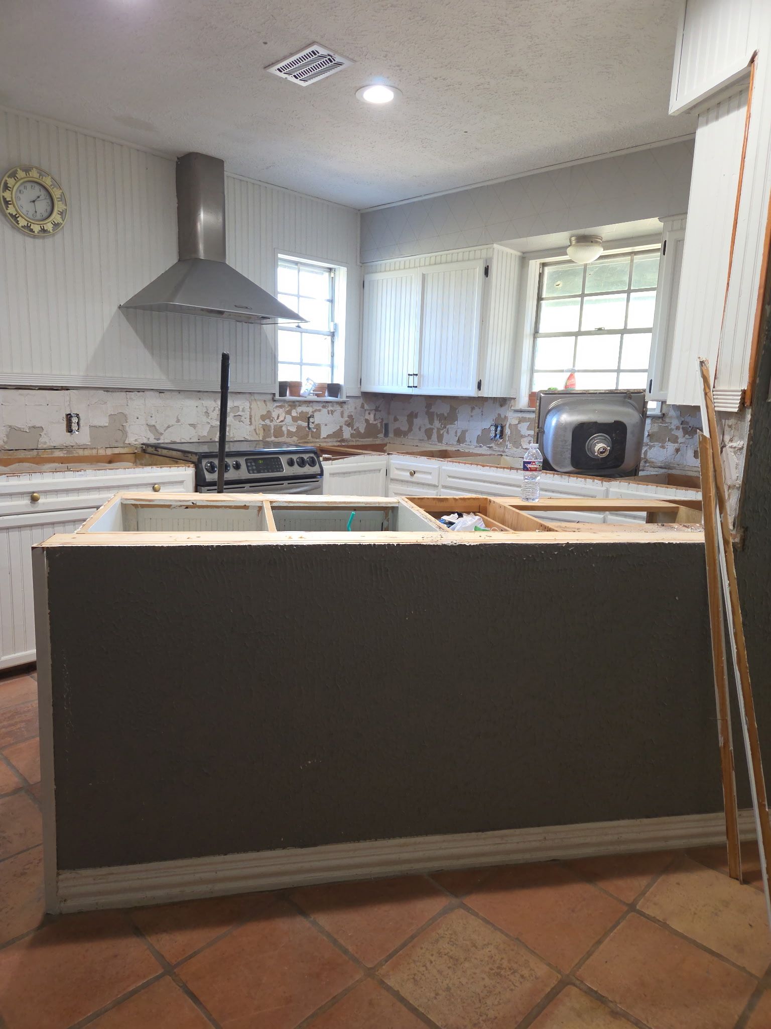 Kitchen remodel in progress, island, cabinets, range hood, and tile floor visible.