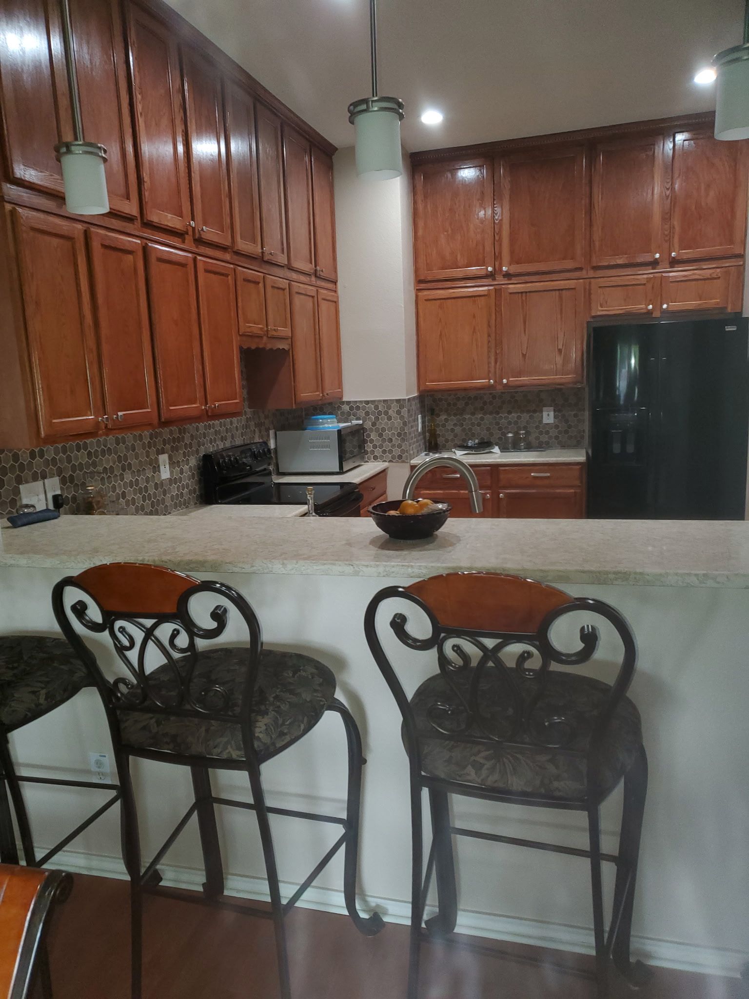 Kitchen with brown cabinets, bar seating, and a black refrigerator.
