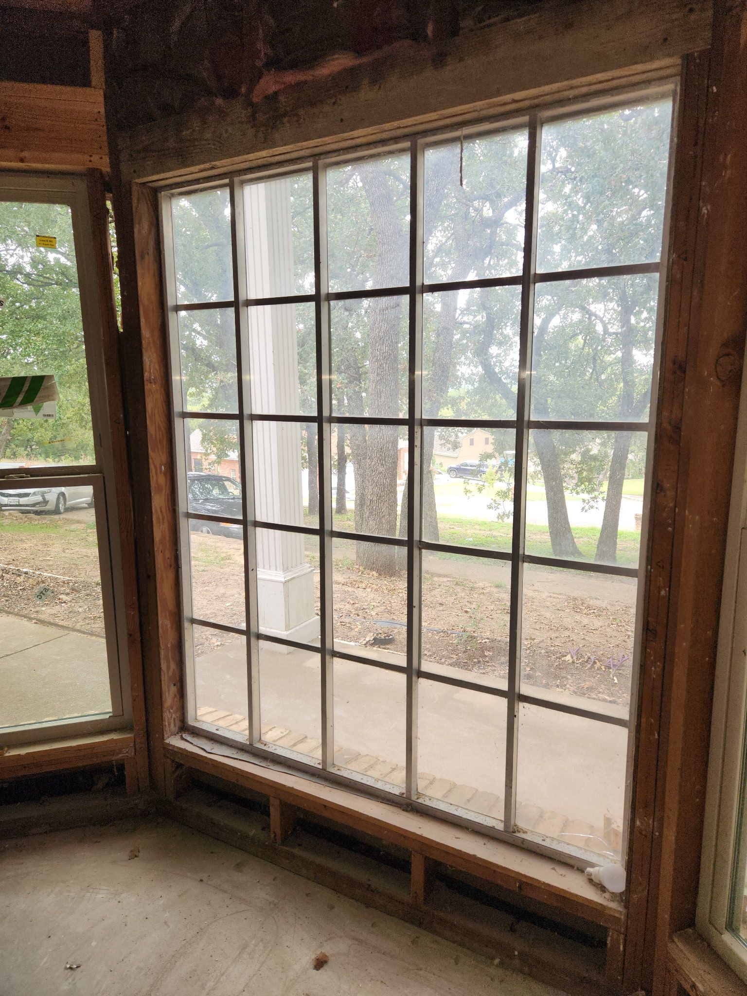 Large grid window in a room under construction, showing a view of trees and a street.