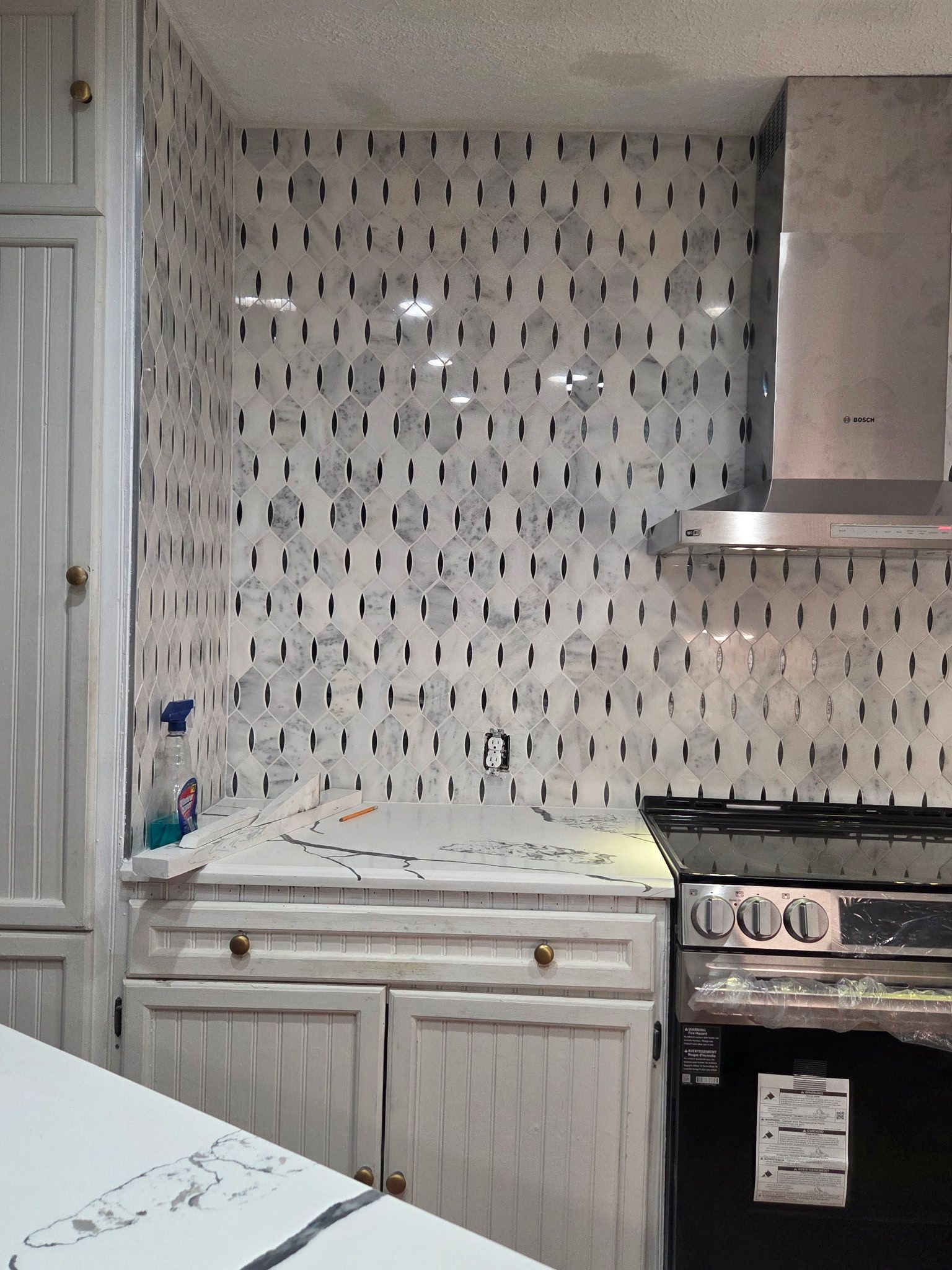 Kitchen with white cabinets, marble backsplash, and stainless steel range hood.