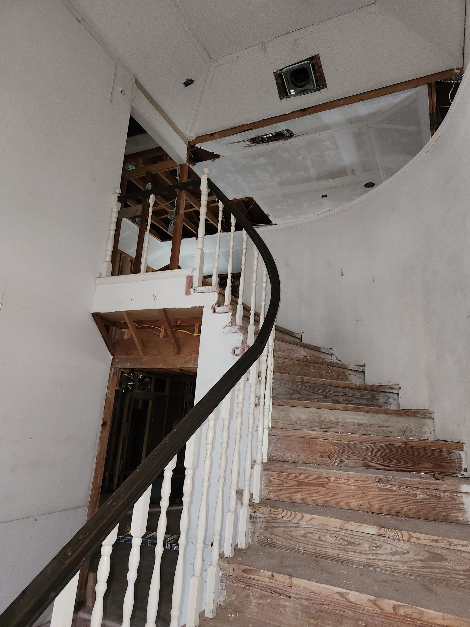 A curved staircase in a dilapidated building with worn wooden steps and a dark handrail.
