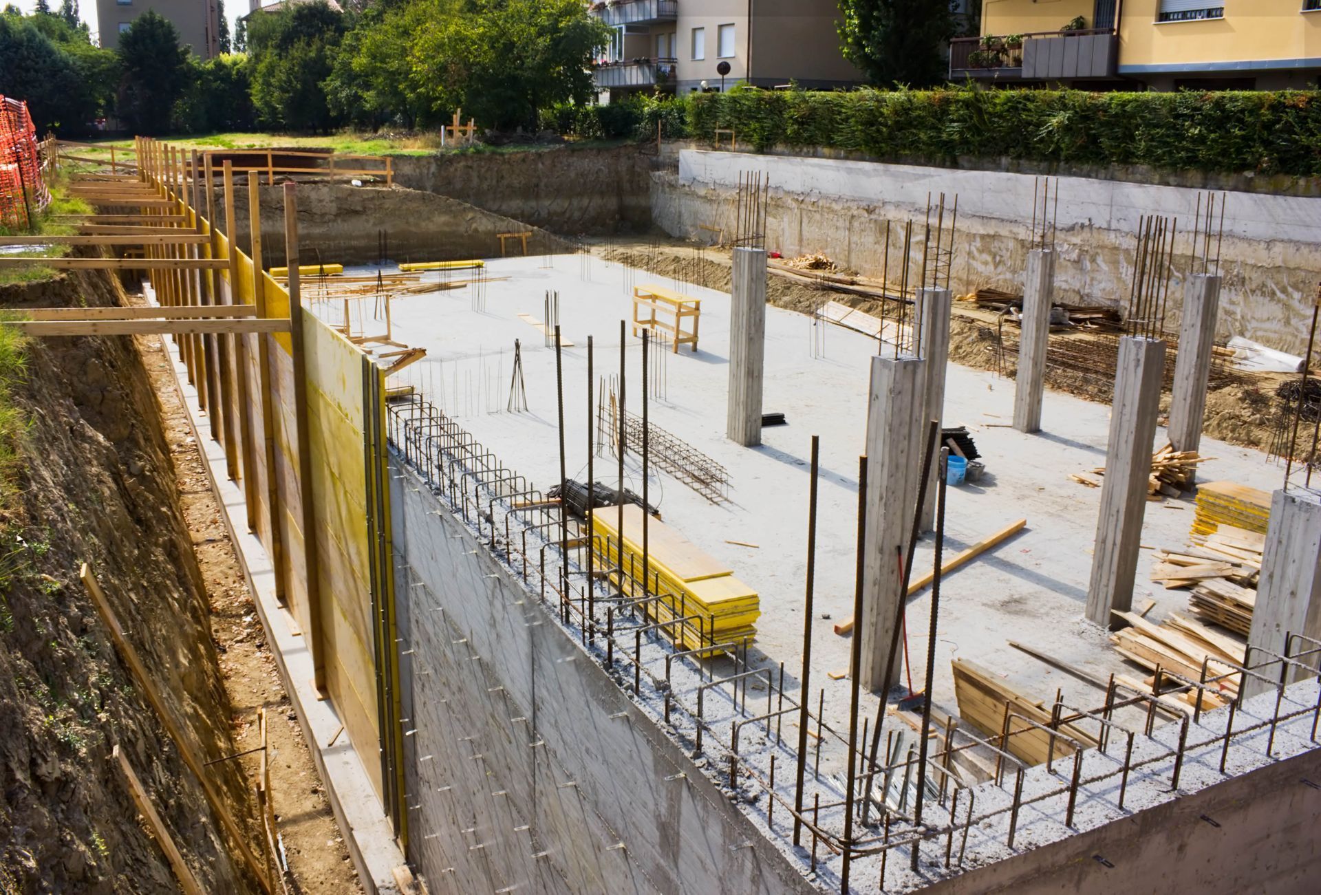 Construction site with concrete foundation, pillars, and exposed rebar, near retaining walls.
