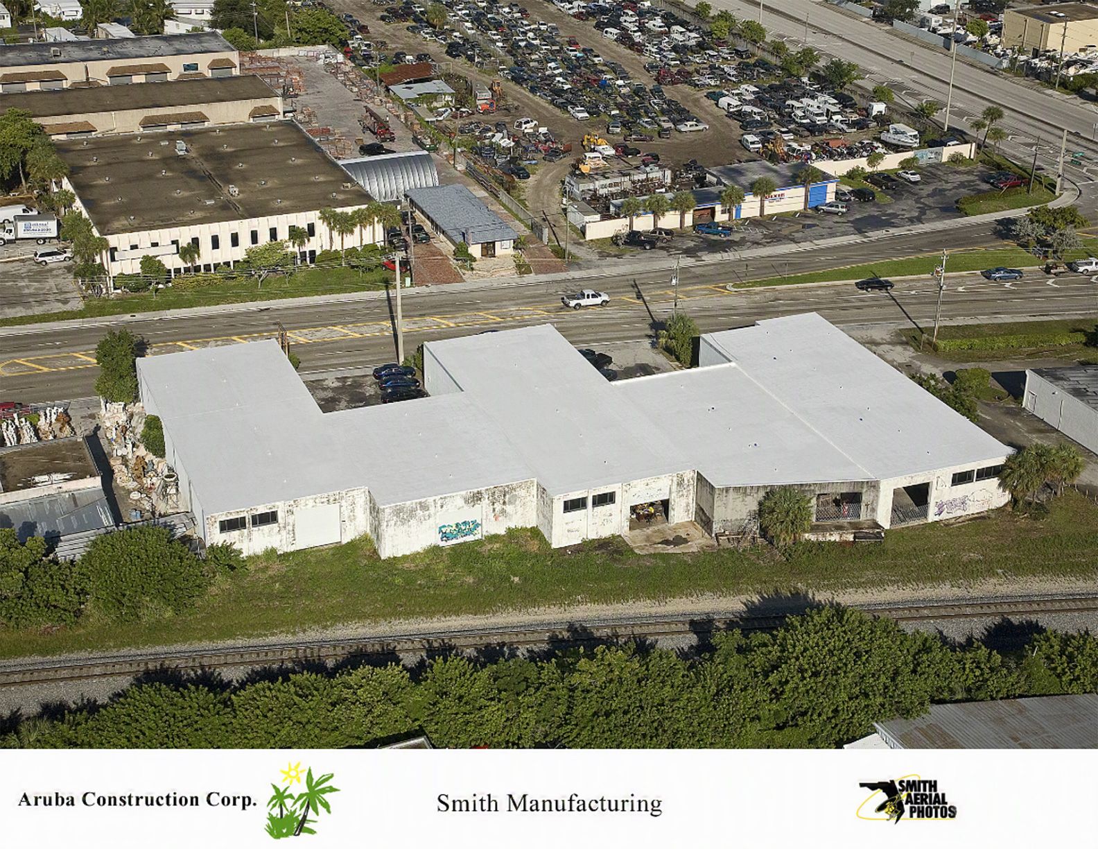 Aerial view of a large white industrial building beside a road and residential neighborhood.