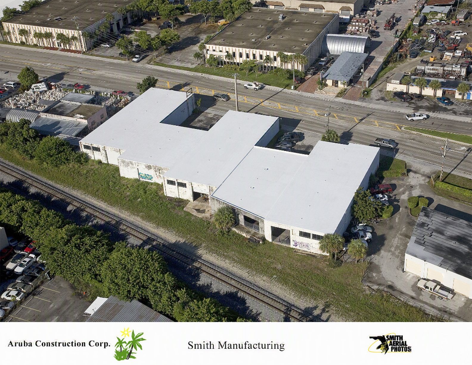 Aerial view of a white-roofed commercial building beside a road and parking lot.