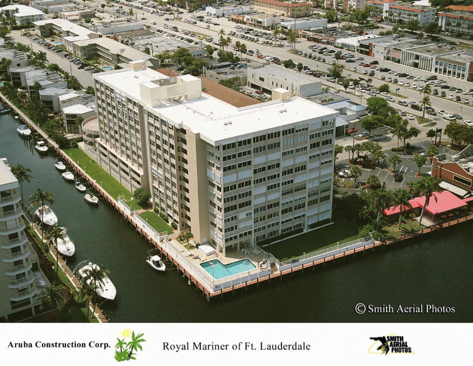 Aerial view of a white waterfront condo with a pool, boats, and nearby streets in Fort Lauderdale.