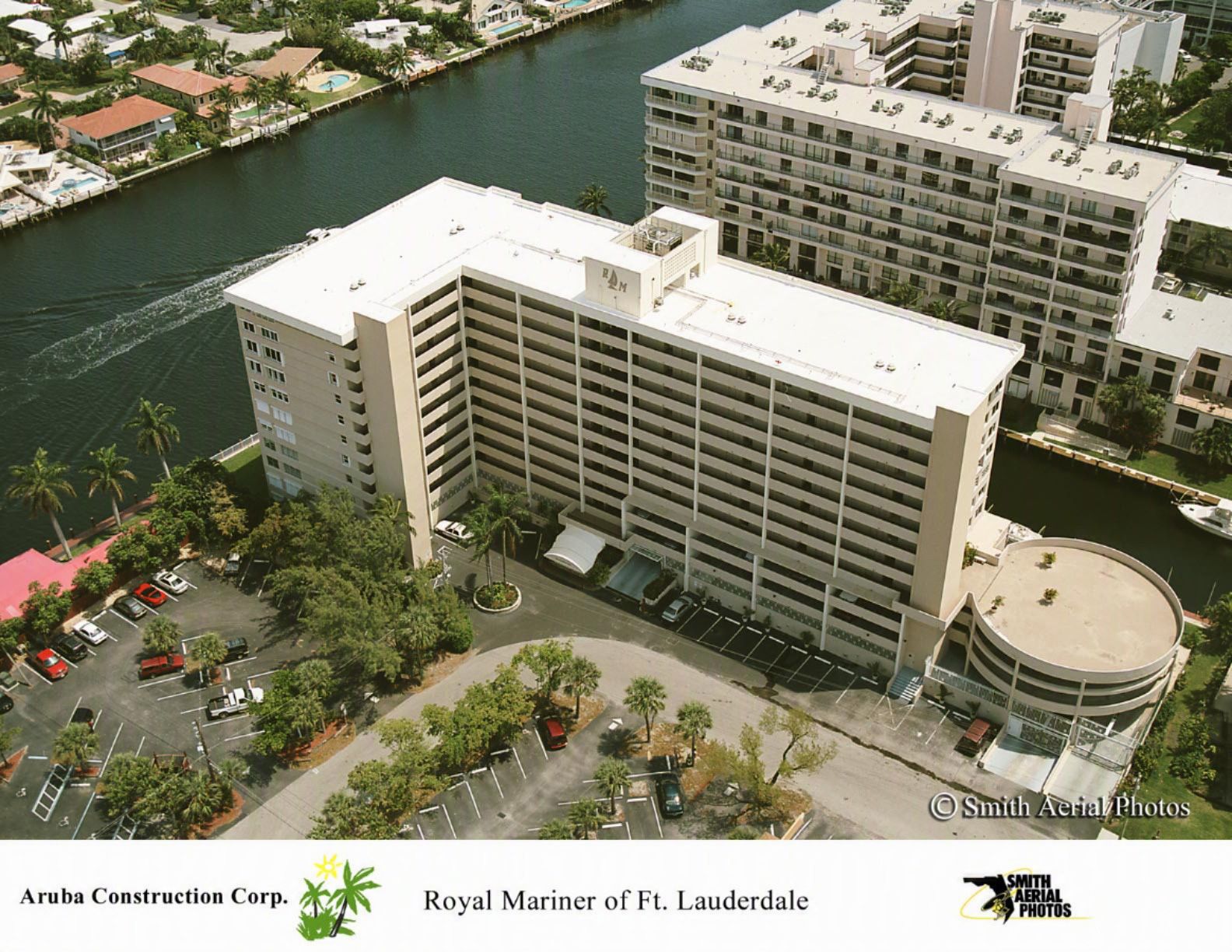 Aerial view of a waterfront hotel complex with beige buildings, a parking lot, and a canal nearby