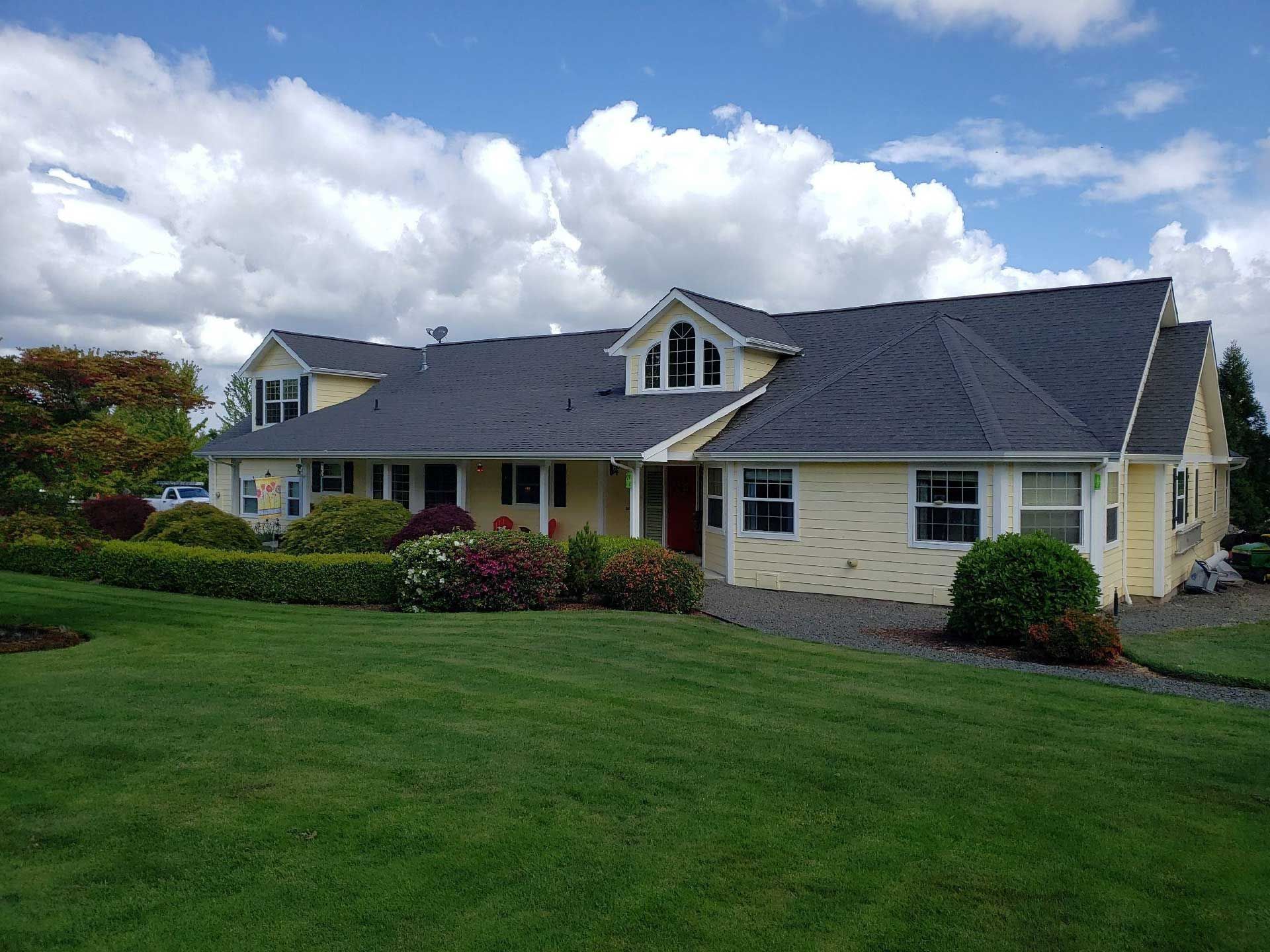 yellow house with black roof, white trim, and a green lawn under a partly cloudy sky