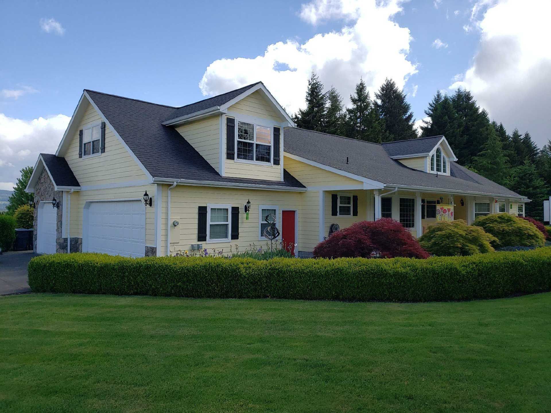 a structure with black shutters, red door, garage, and green lawn on a sunny day