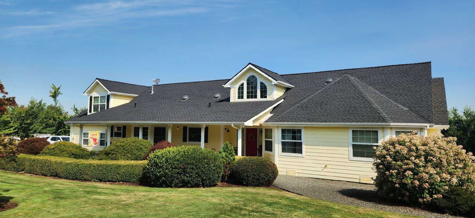 a yellow house with dark roof and landscaping under a blue sky