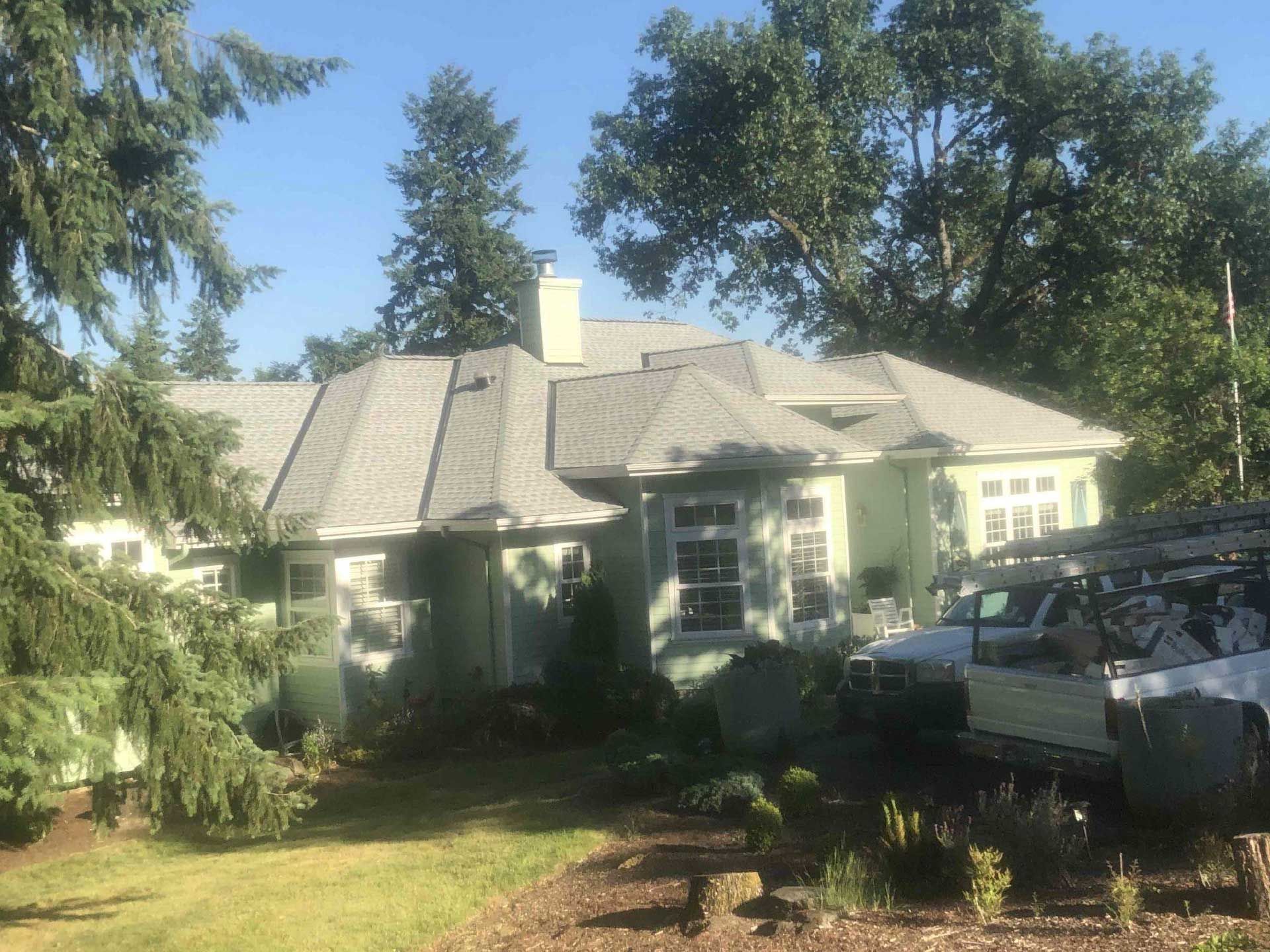 a light yellow house with gray roof, surrounded by trees and a white truck
