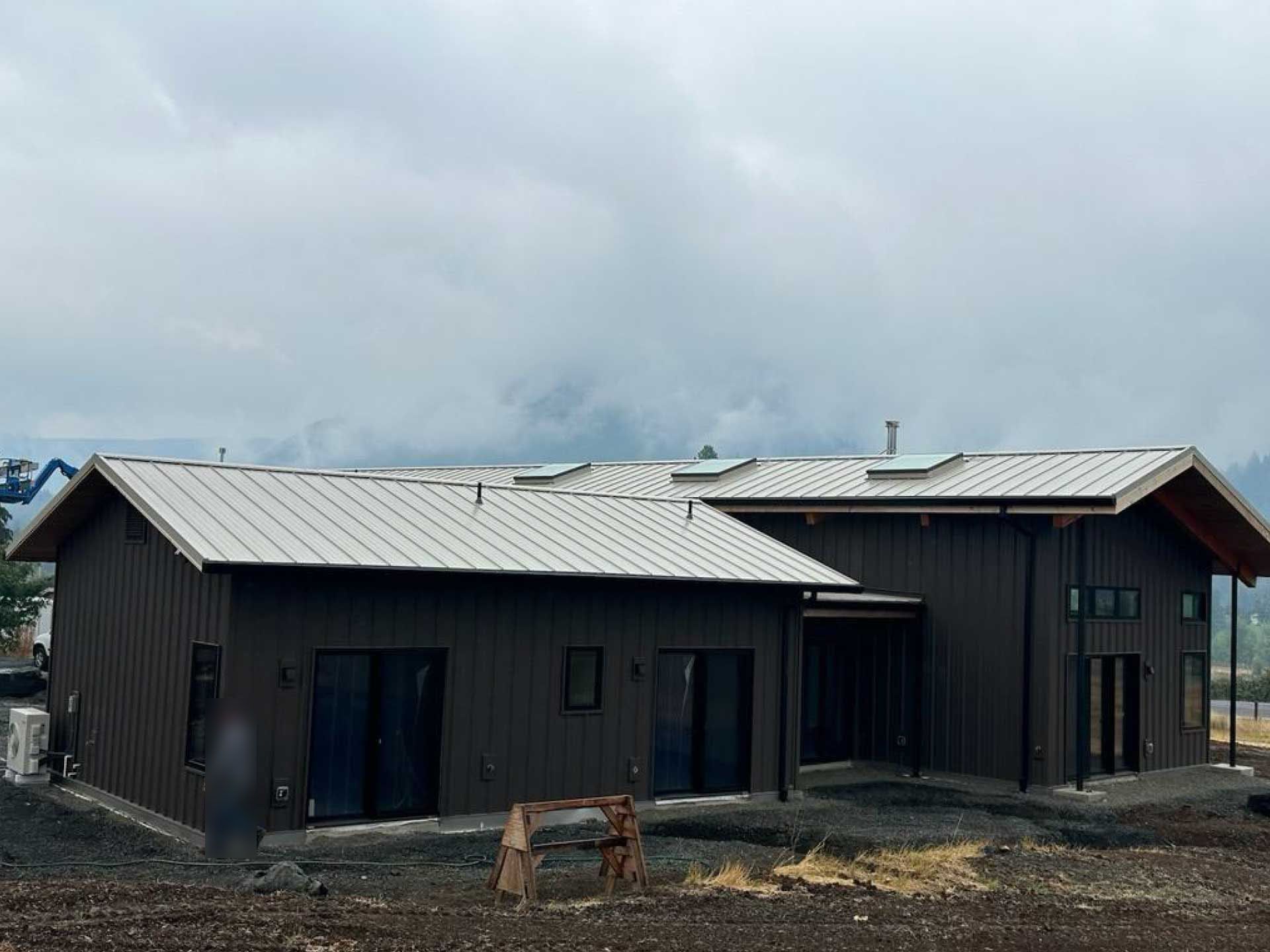 modern, brown-sided house with metal roof against a cloudy sky
