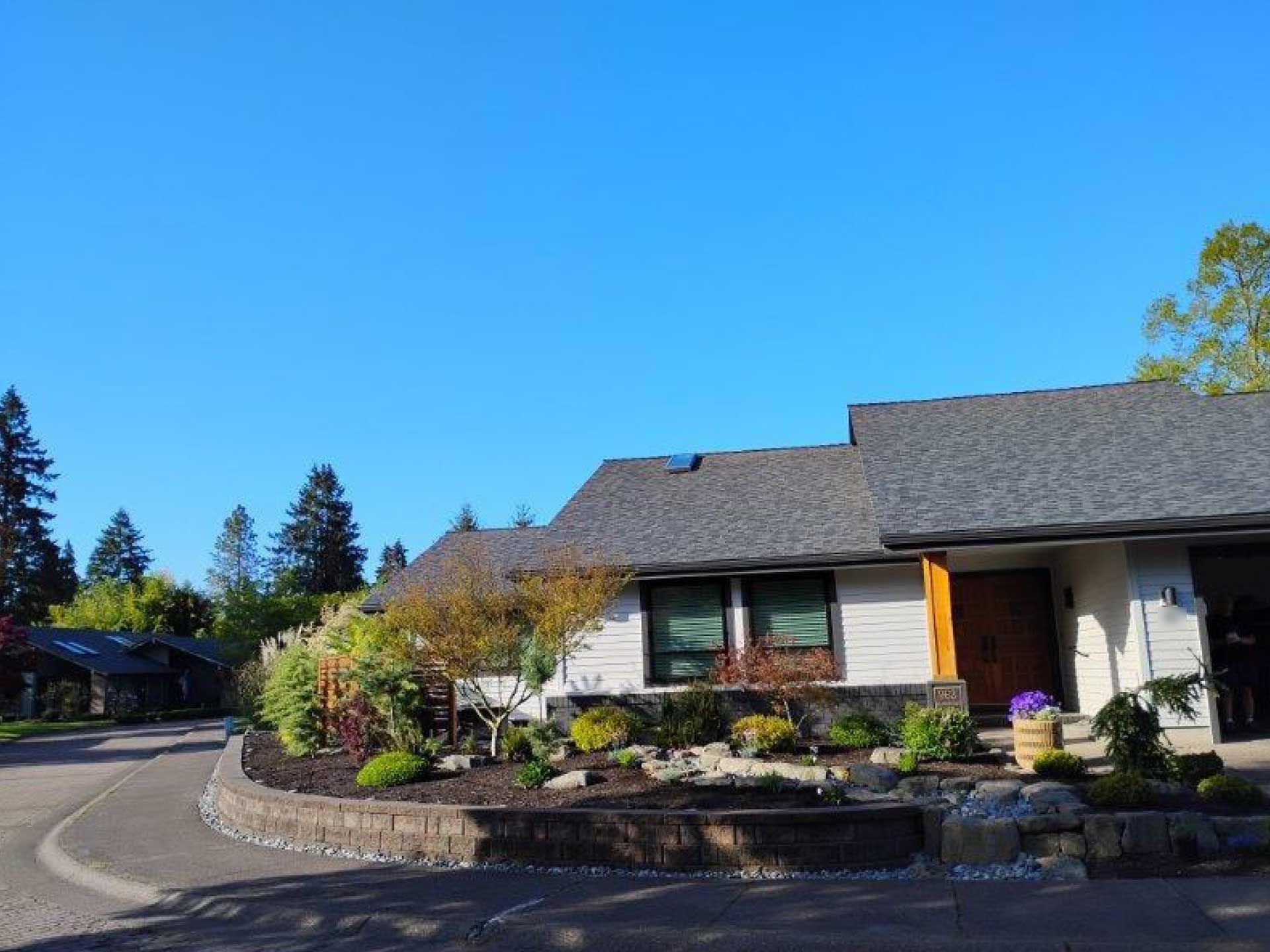 house with dark roof, white siding, and landscaped yard under a bright blue sky