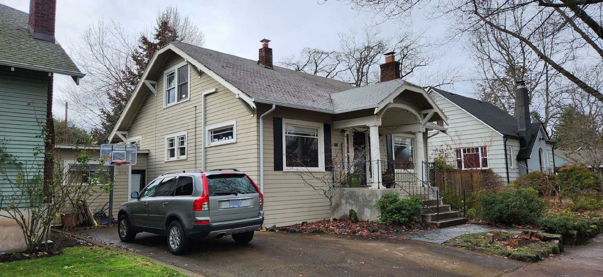a light-colored house with a dark gray SUV parked in the driveway on a cloudy day