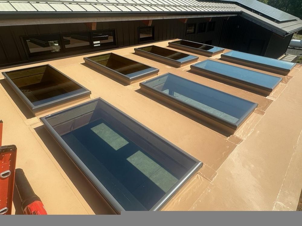 Skylights installed on a brown roof, varying in size and shape with metal frames. A level is partially visible.