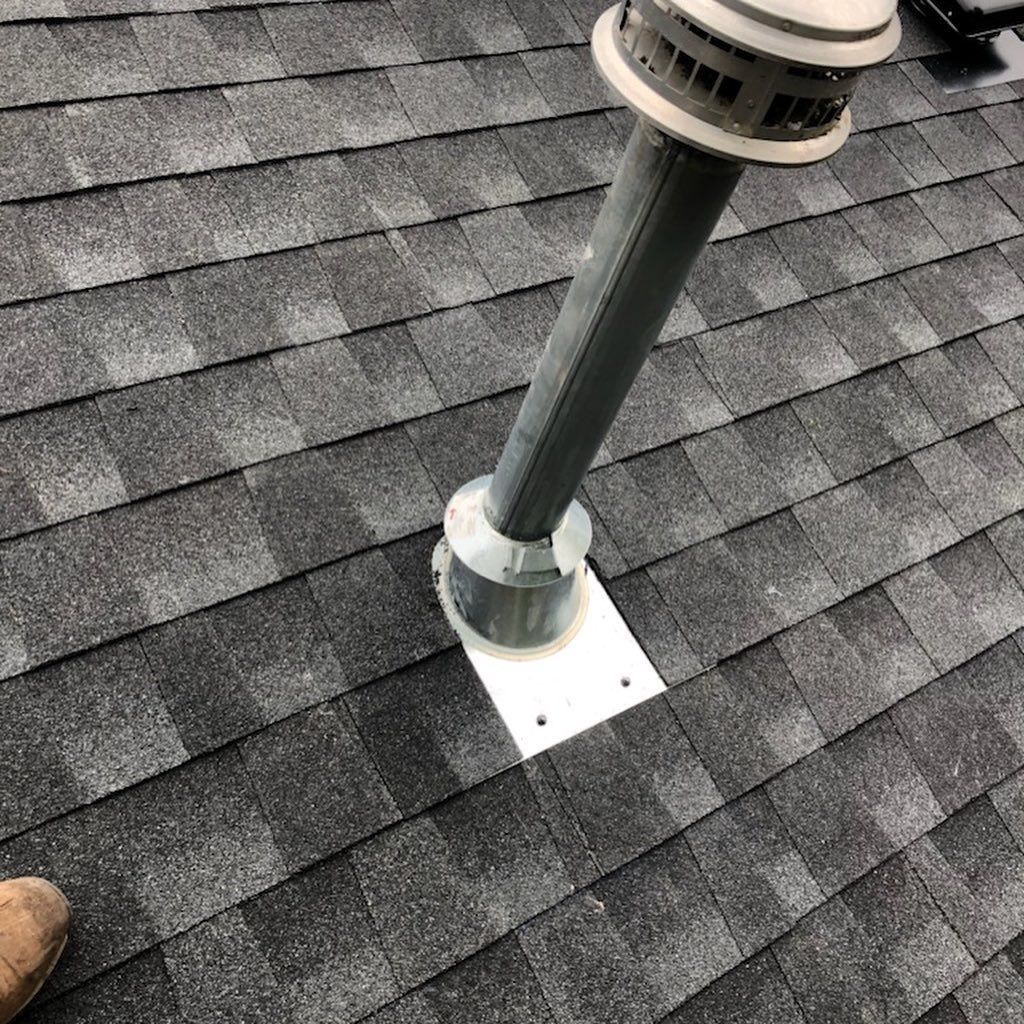 A gray vent pipe on a dark gray shingled roof with a white base.