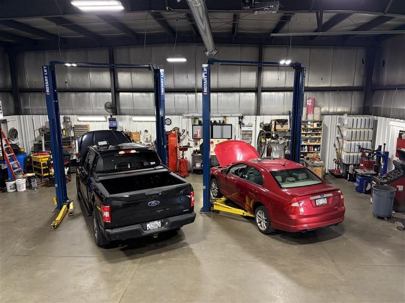 Two vehicles on lifts in a garage; a black truck and a red car. Tools and equipment are in the background.