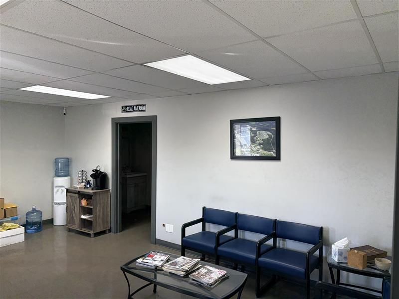 Waiting room with blue chairs, coffee station, water cooler, magazines, and framed art.