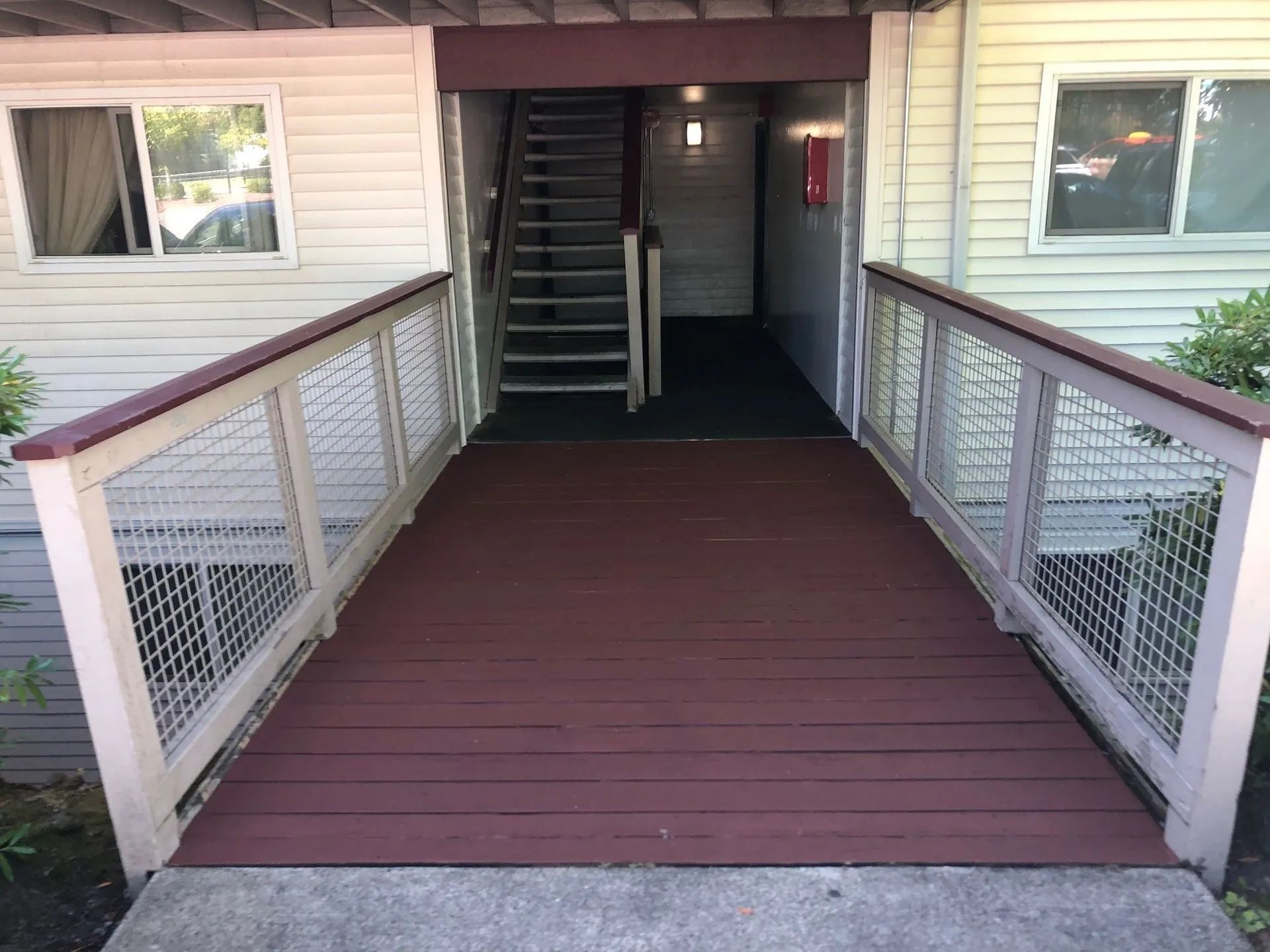 Ramp leading to an apartment entrance with a staircase, painted red and white, flanked by a railing.