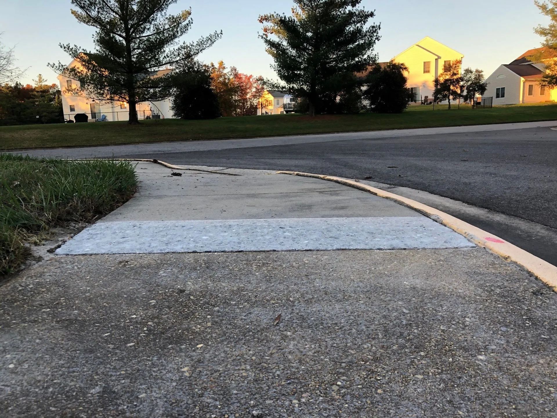 Concrete sidewalk with a white-painted section, curb, and asphalt road in a suburban setting.