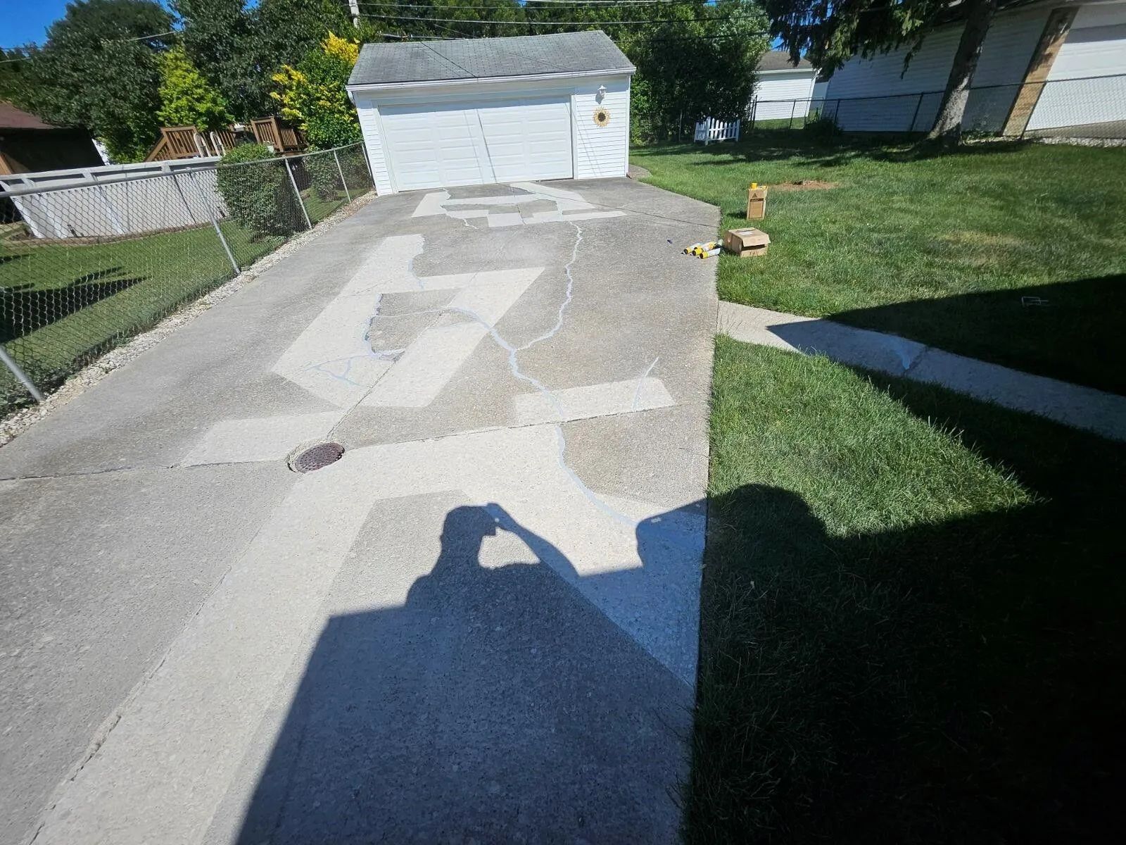 Concrete driveway with paint design, leading to a garage. Sunlit with grass, fence, and a shadow.