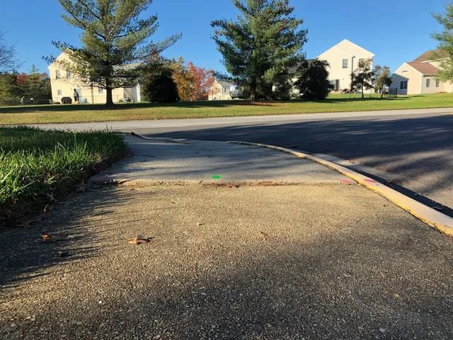 Sidewalk and street corner in a residential area, with grass and houses in the background.