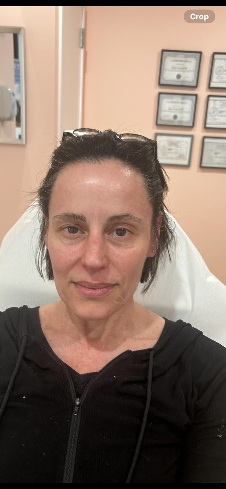 A woman without makeup is sitting in a chair in a room.