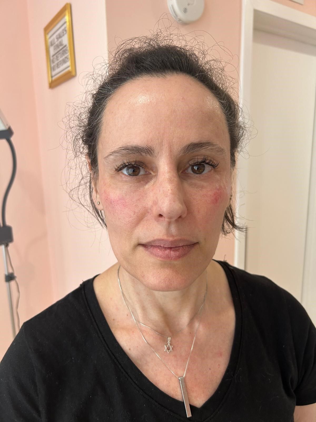 A woman wearing a black shirt and a necklace is looking at the camera.