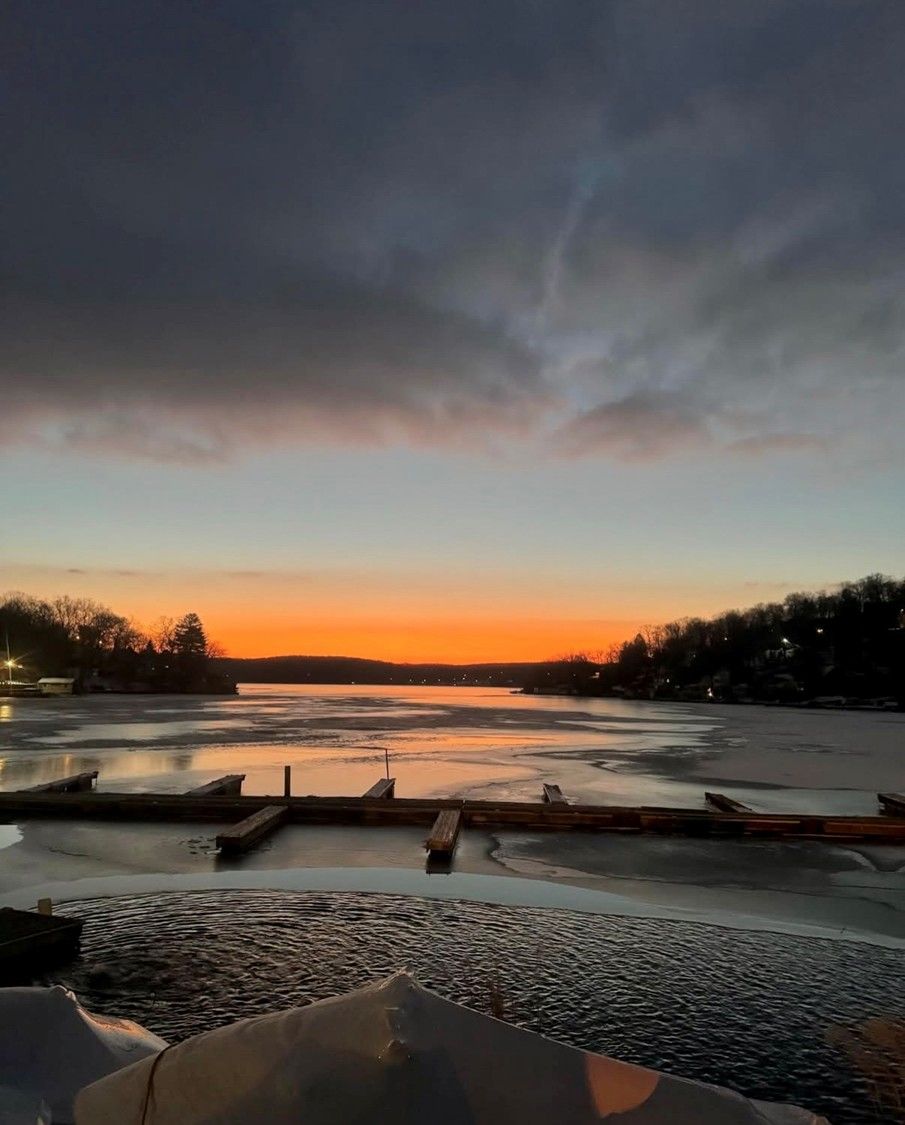 Sunset over a frozen river, with dark clouds and wooden docks silhouetted in the foreground